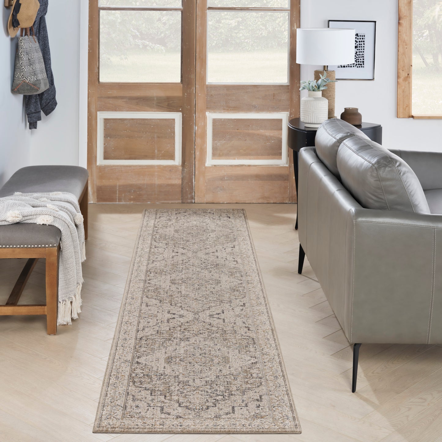 Beige distressed-pattern rug runner on light wood floor, flanked by gray sofa and entry bench in a modern rustic living area.