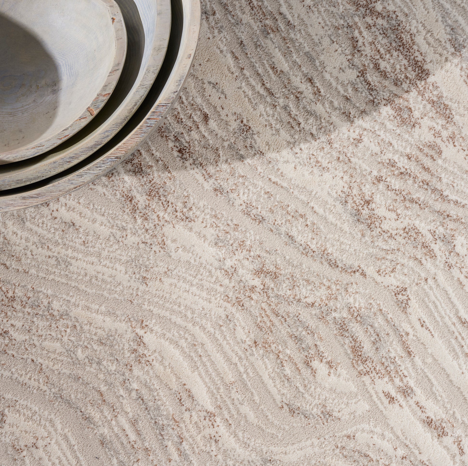Beige textured rug with light brown wavy stripes; gray cylindrical rolls stacked in the top-left corner.
