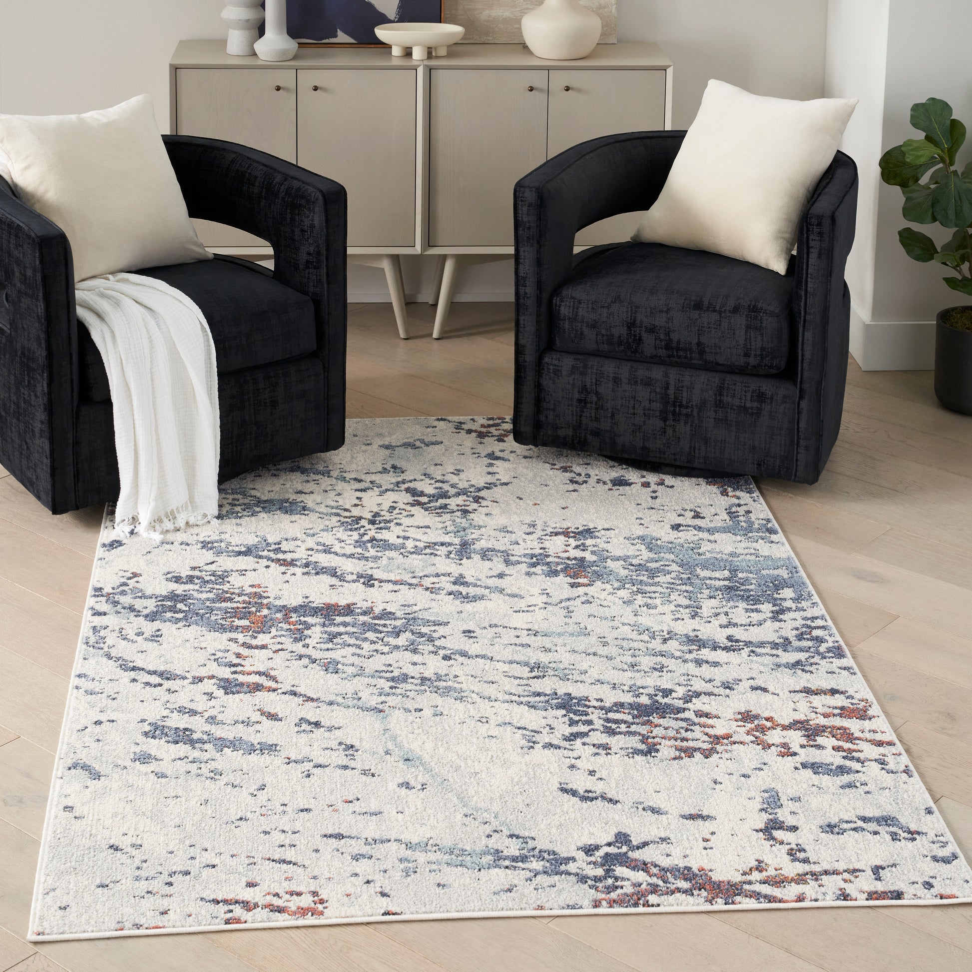 Two black velvet armchairs with cream cushions flank a light abstract blue-gray rug in a modern living room with a sideboard.