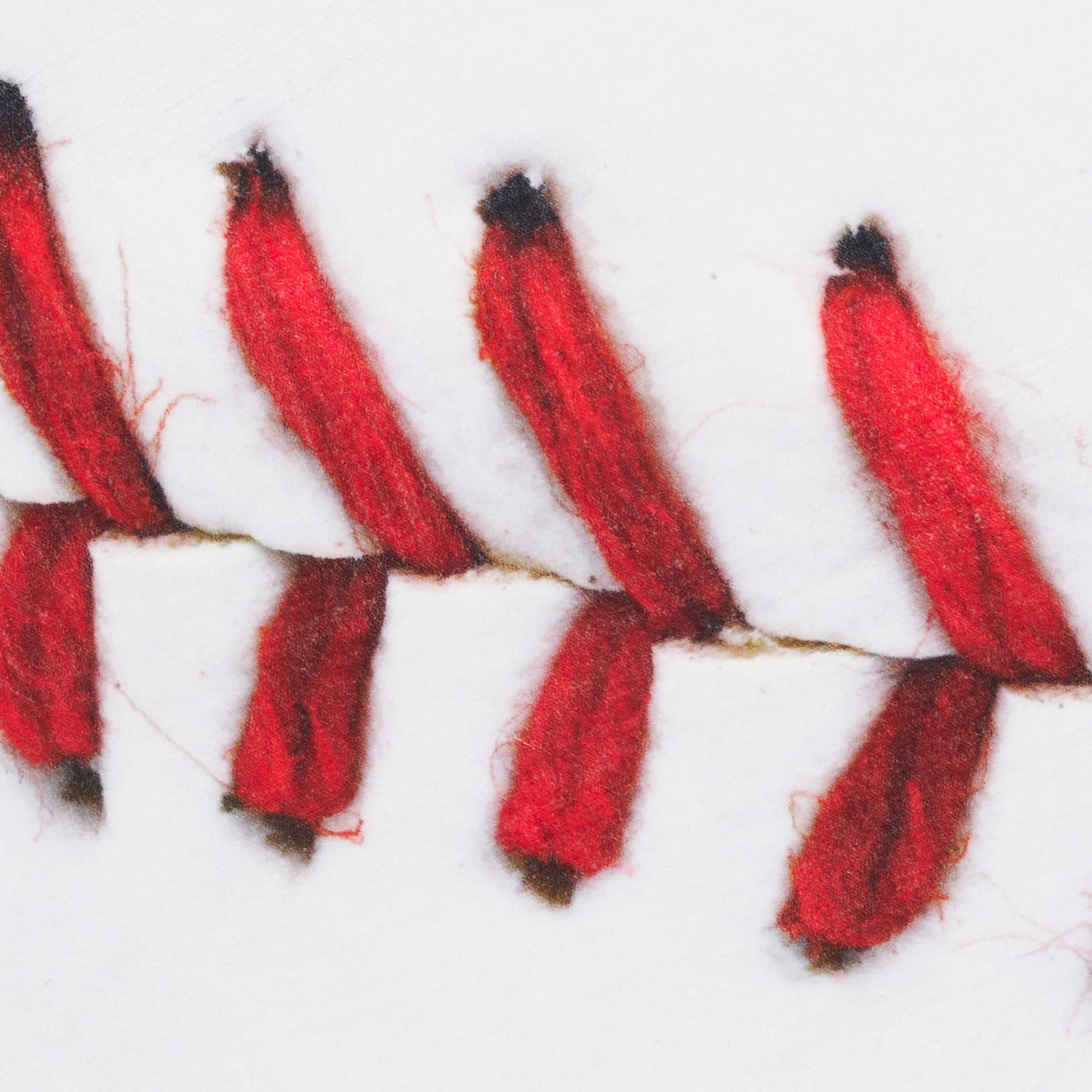 Close-up of red thread chain-stitch embroidery along a white rug seam with dark-tipped stitches.