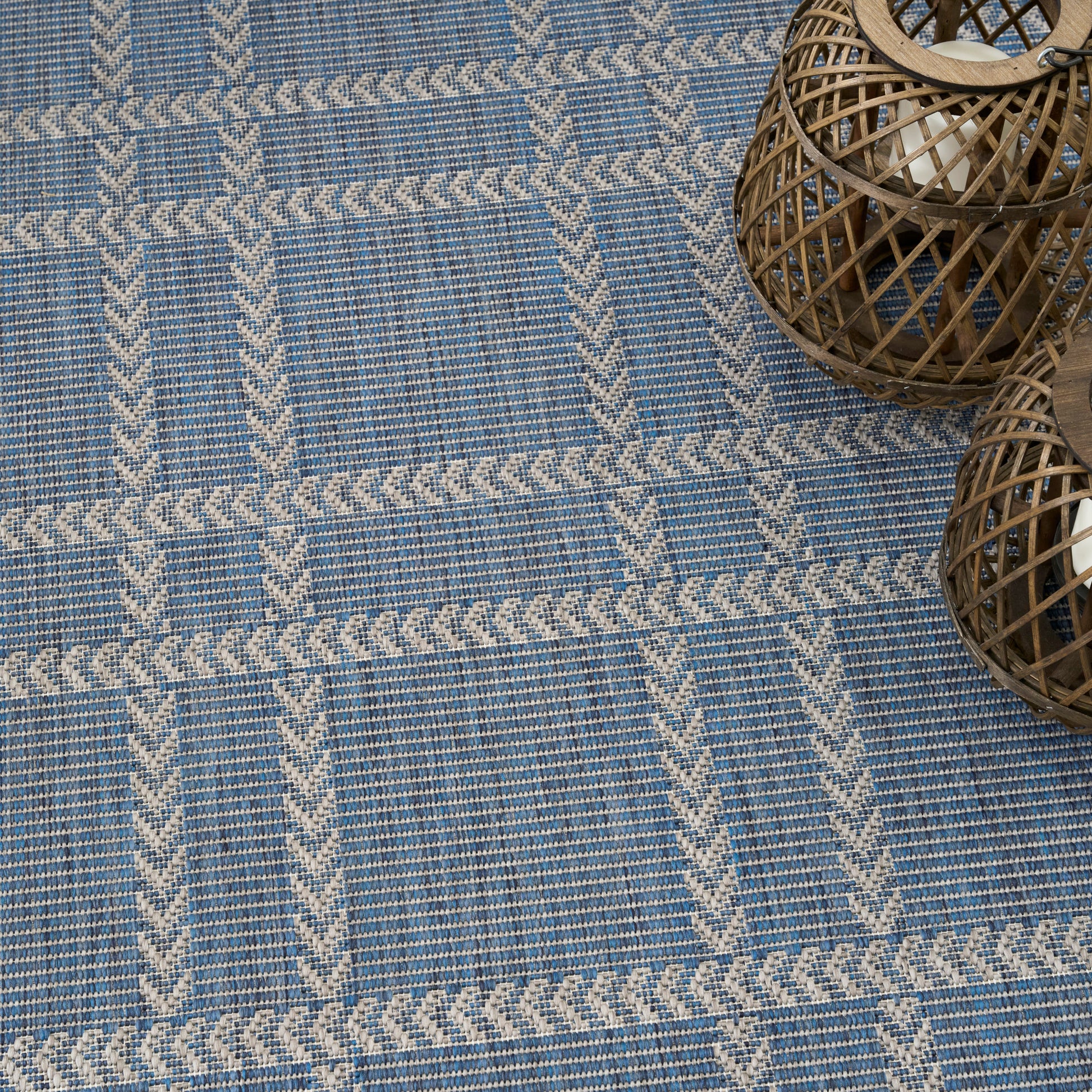 Blue woven rug with cream braided stripe grid pattern; natural wicker lanterns in the top-right corner.