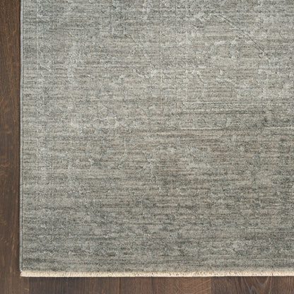 Rectangular grey textured rug with subtle pattern and light fringe along the bottom edge on dark wood floor.