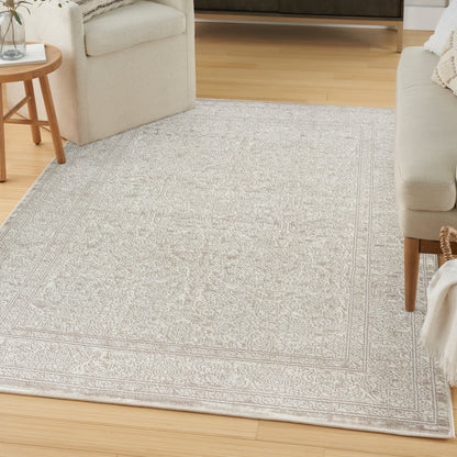 Light gray rectangular area rug with an intricate border pattern in a living room with beige sofa and round wooden side table