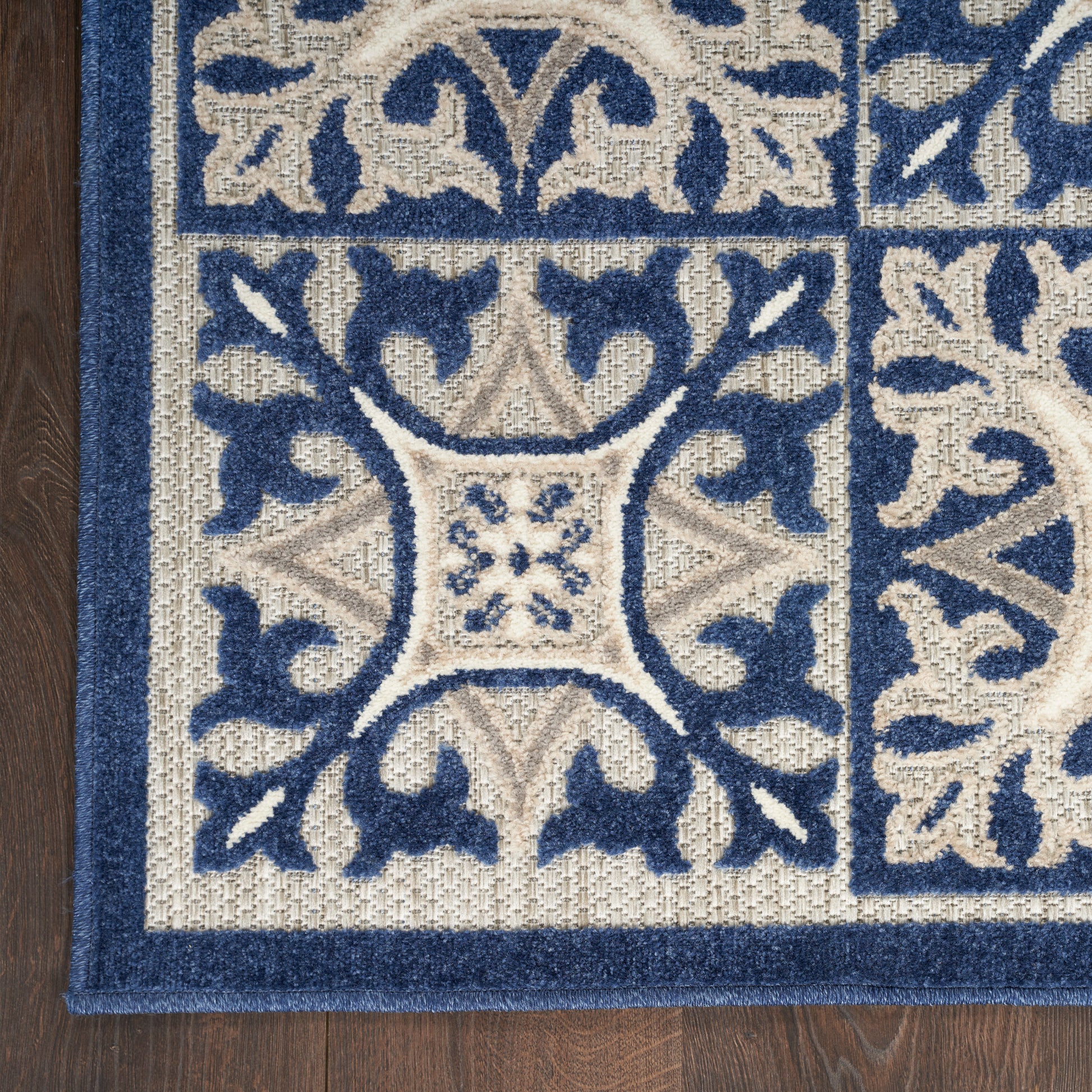 Blue and cream patterned area rug with ornate scrollwork and a central square motif, dark blue border on a wood floor.