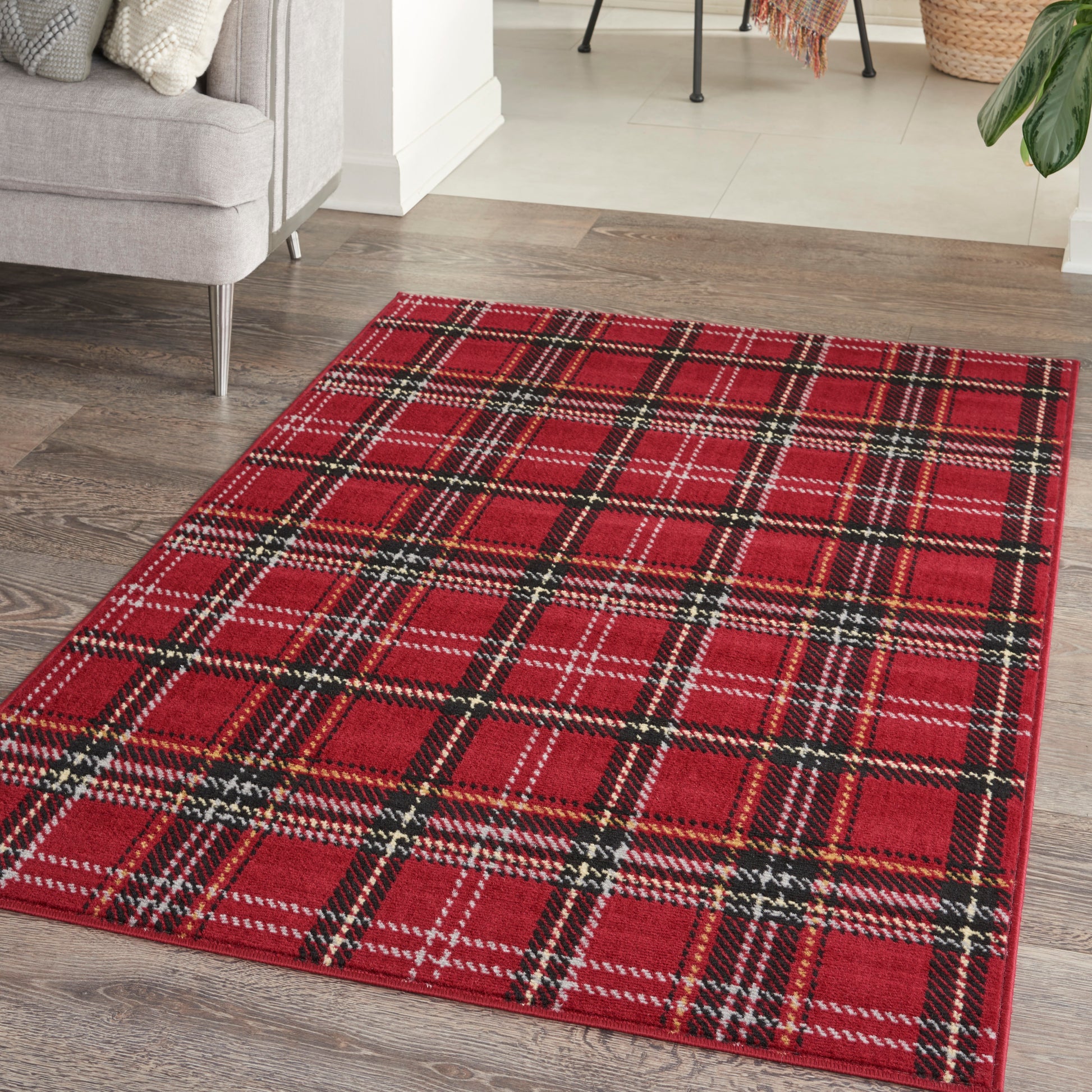 Red tartan plaid rectangular rug with black, white and yellow lines on a dark wood floor beside a gray sofa.
