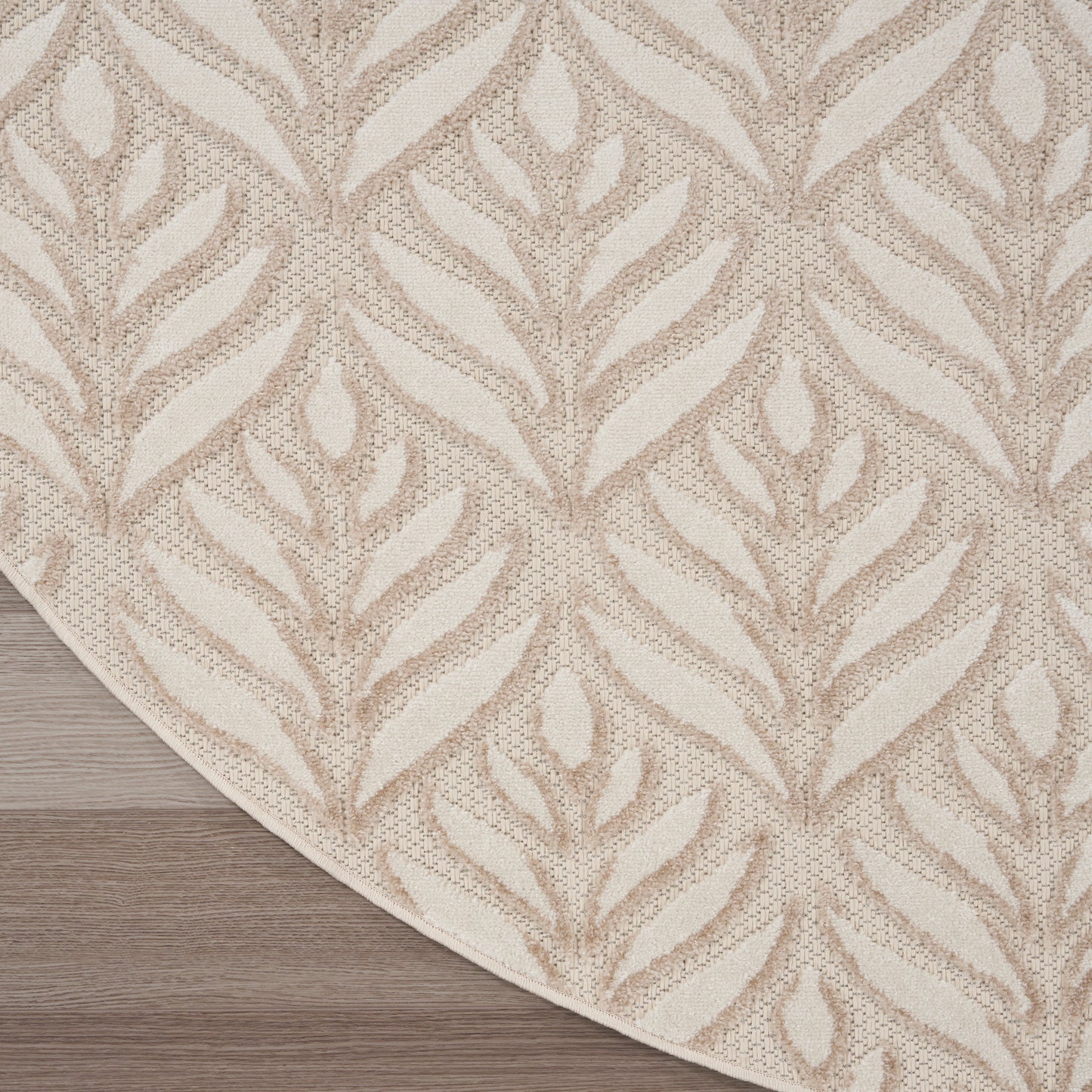 Beige area rug with cream leaf/fern pattern and curved edge on light wood floor.