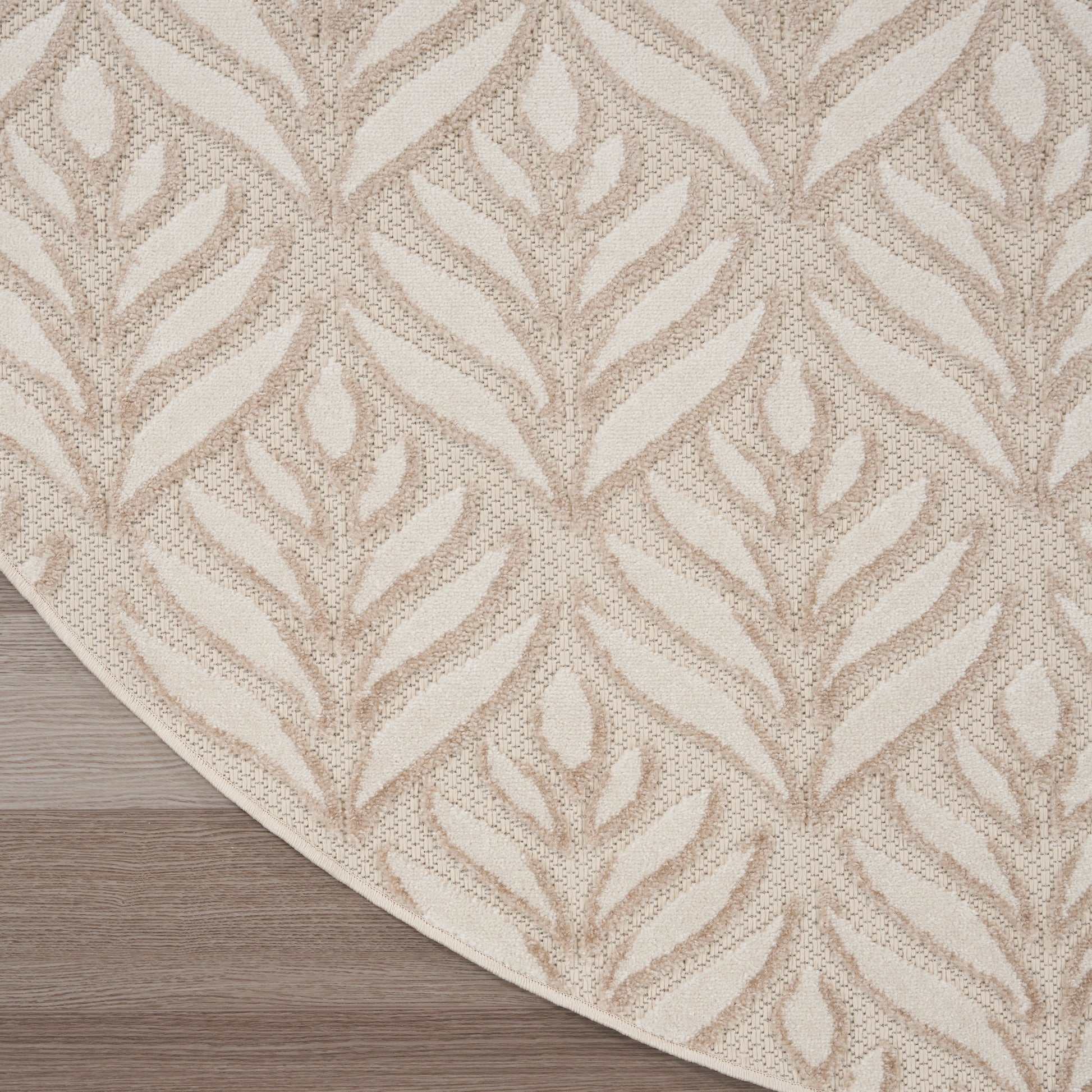 Beige area rug with cream leaf/fern pattern and curved edge on light wood floor.