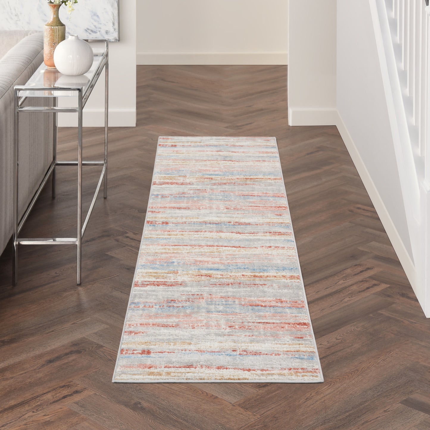 Long distressed multicolor runner rug with cream, blue and orange stripes along hallway beside a glass-topped console table.