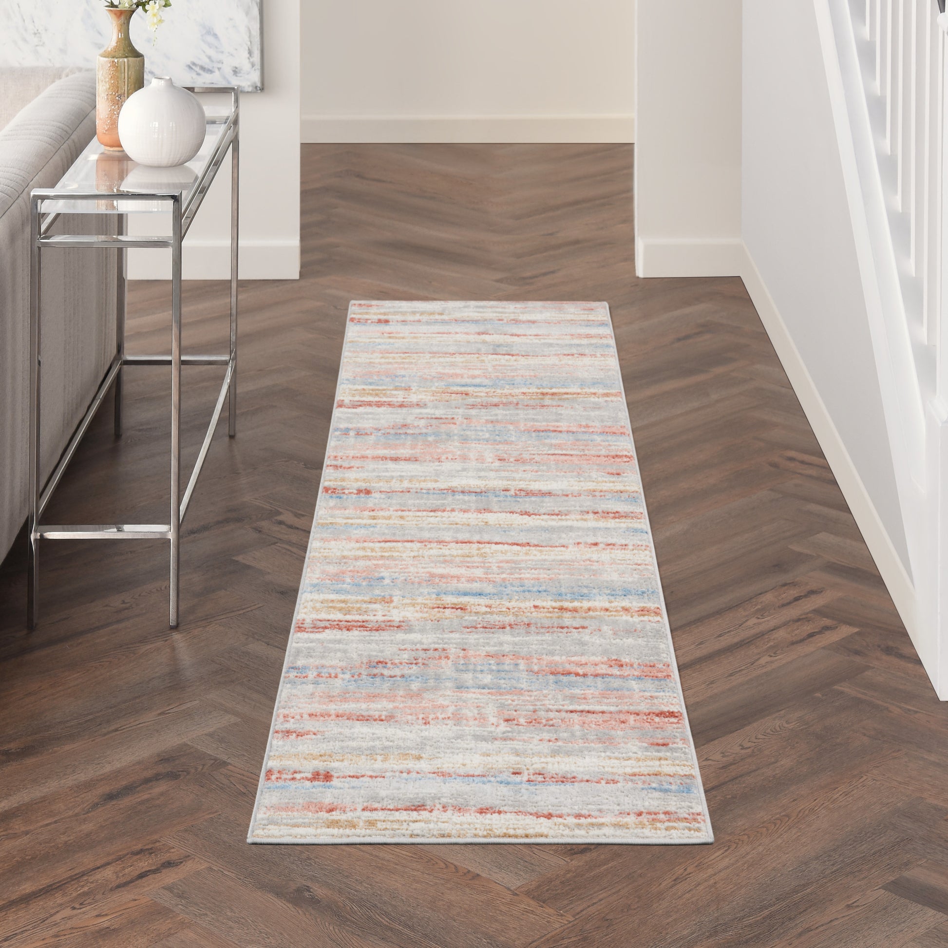 Long distressed multicolor runner rug with cream, blue and orange stripes along hallway beside a glass-topped console table.