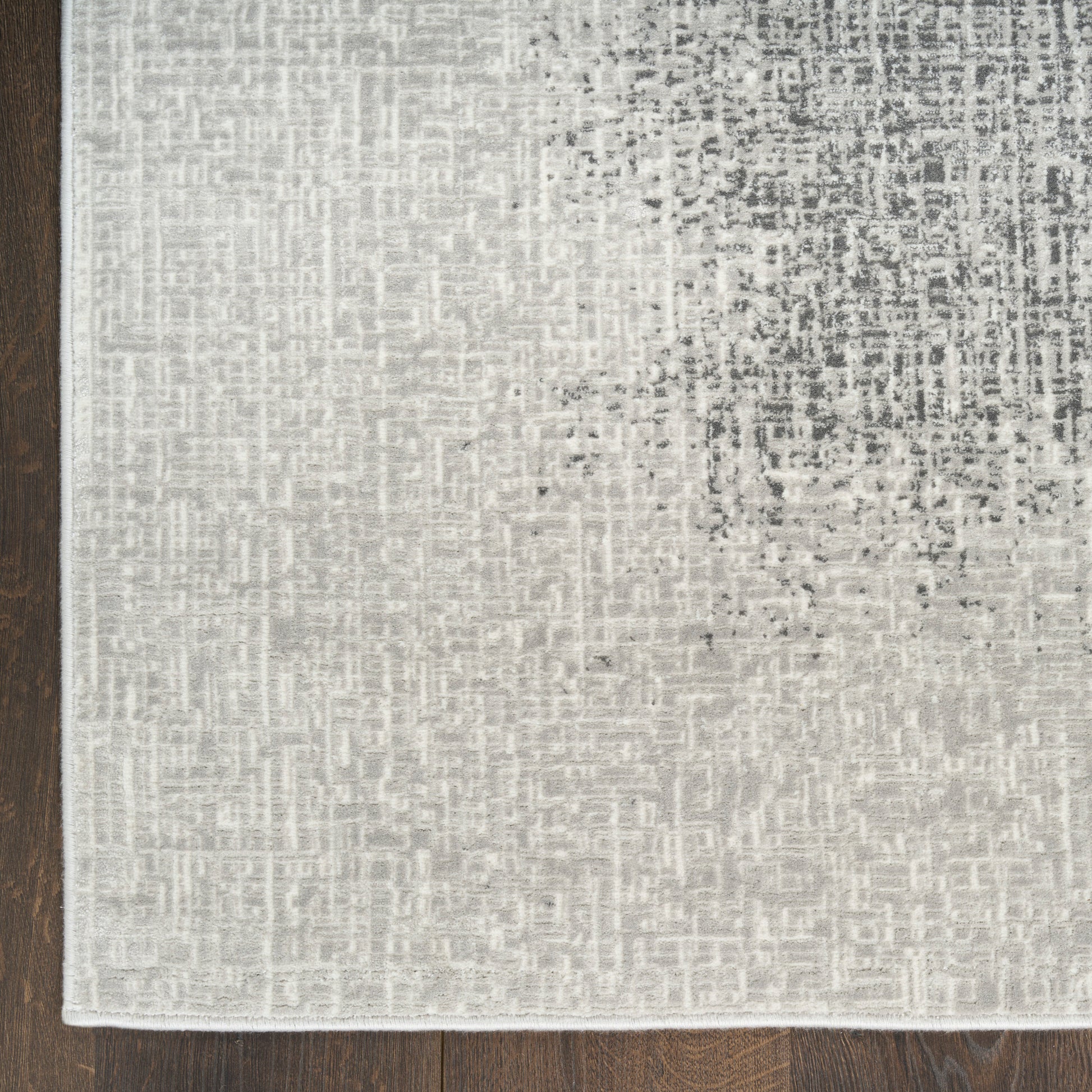 Light gray area rug with subtle textured pattern on dark wood floor.