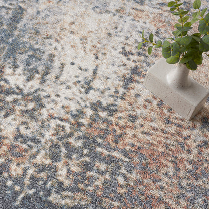 Beige ceramic vase with green sprigs rests on a round abstract patterned area rug in cream, blue and rust.