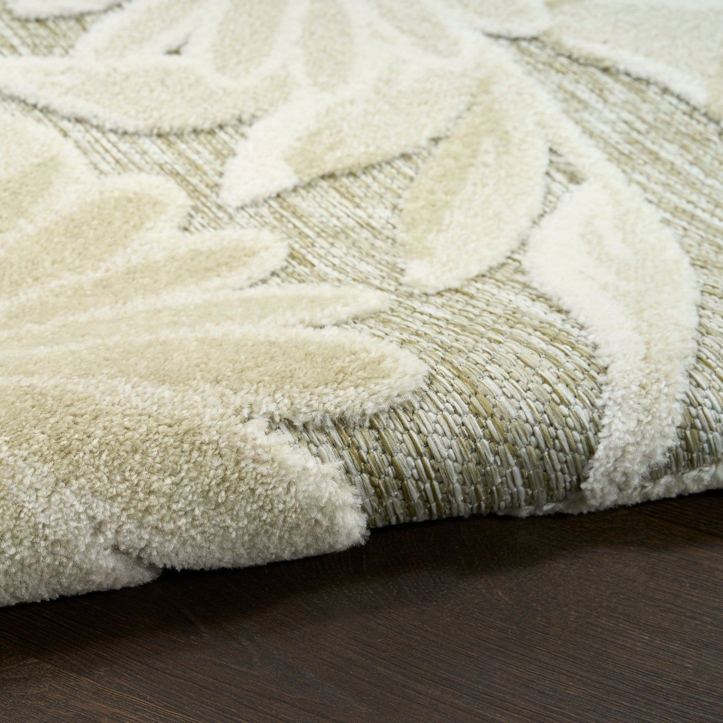 Cream outdoor rug with a raised leaf pattern on a beige woven base, soft plush texture on a dark wood floor.