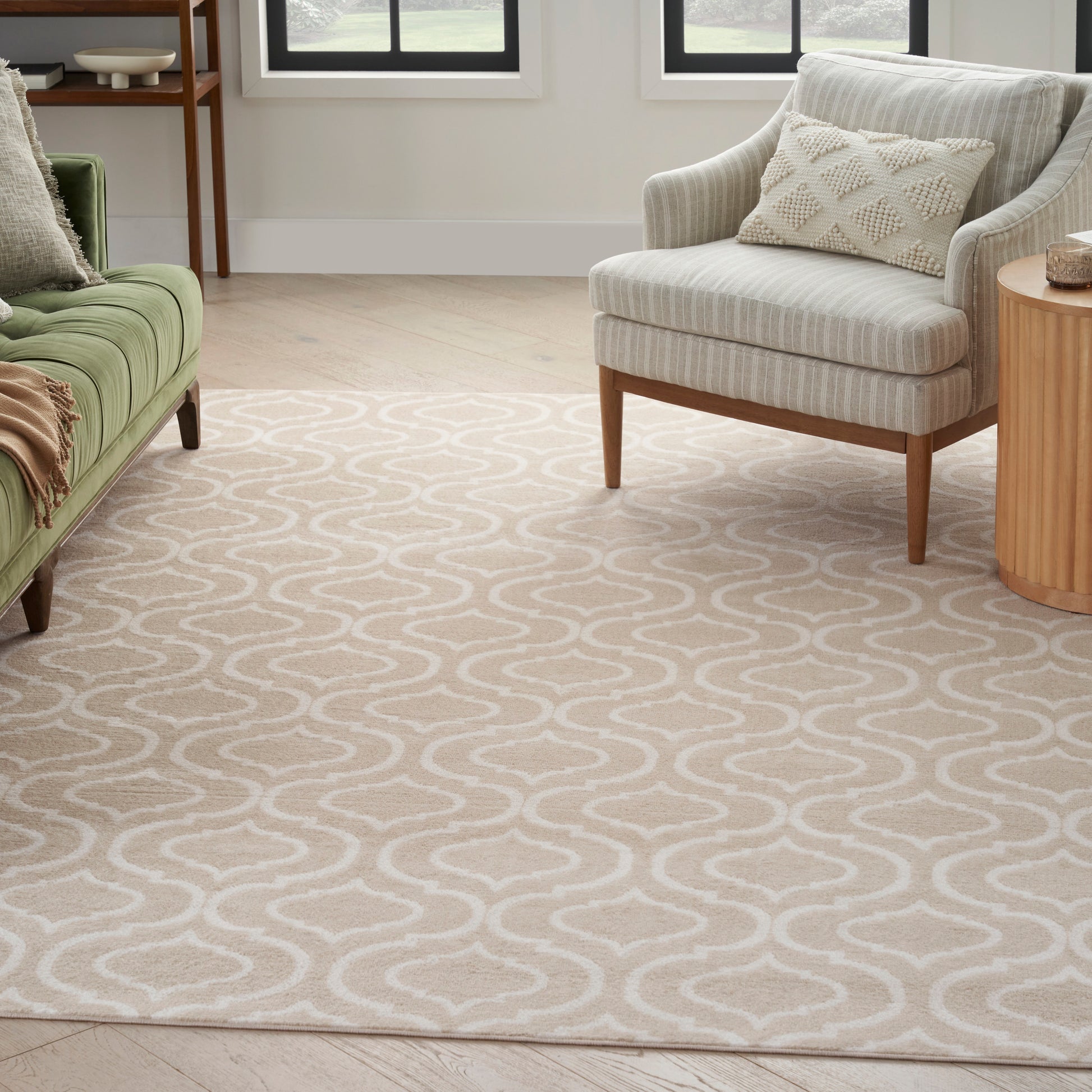 Beige area rug with white wavy trellis pattern, living room with green sofa, grey armchair, wooden side table.