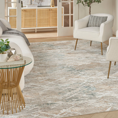 Beige-blue distressed area rug in a modern living room, flanked by cream boucle armchairs with wooden legs and a glass-top side table with a gold spindle base.