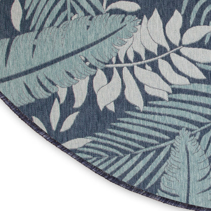 Round rug with teal and light blue tropical leaves on navy background; dark blue binding and fringed edge.