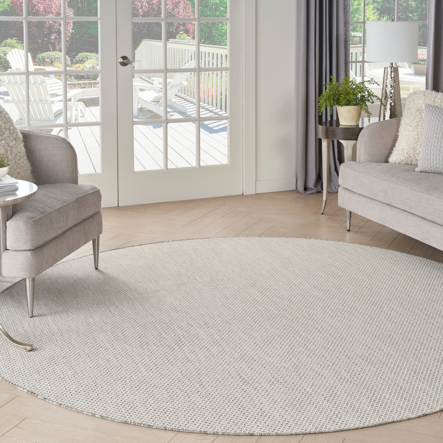 Circular light beige rug in a bright modern living room with gray sofa, armchair, plant, curtains, and glass patio doors.