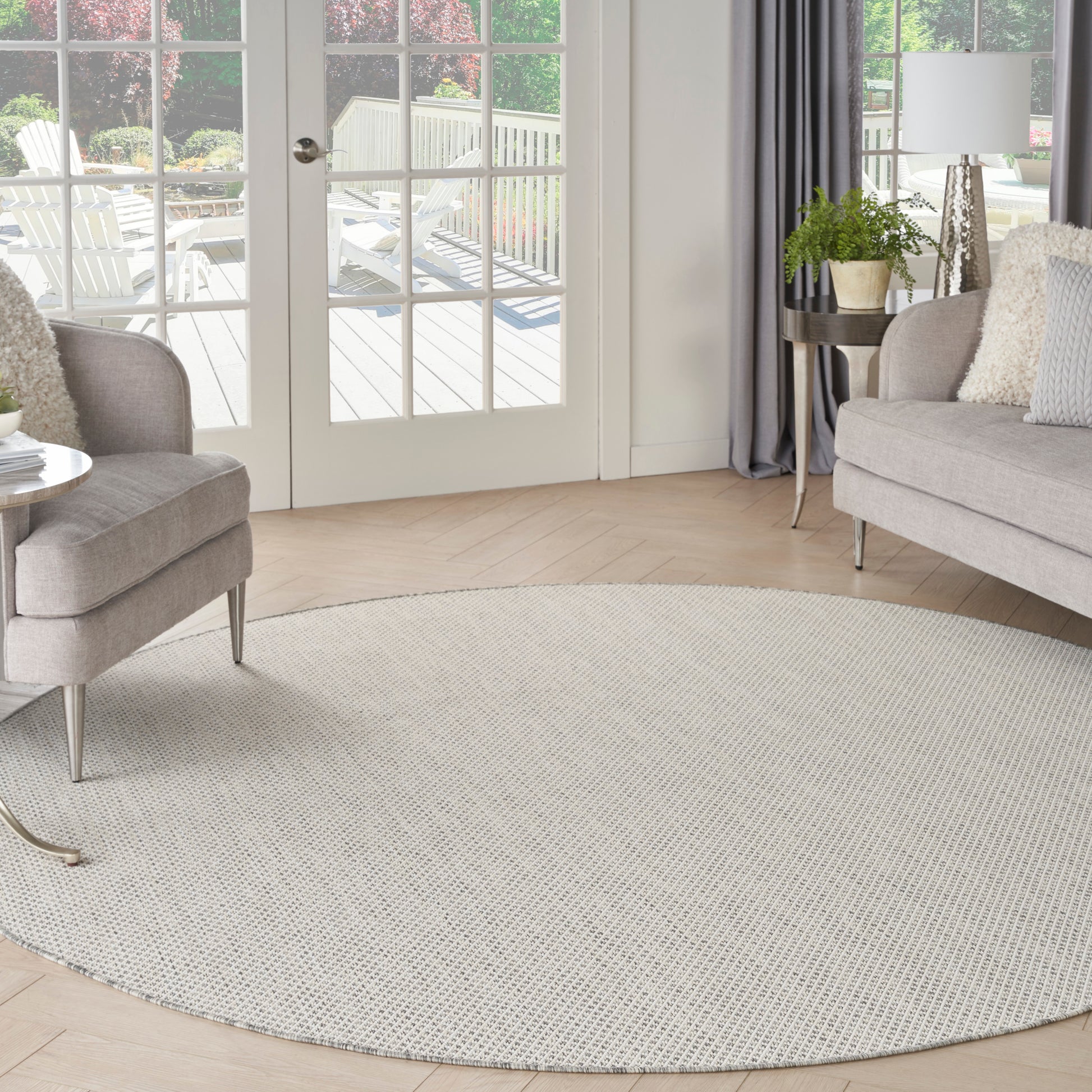 Circular light beige rug in a bright modern living room with gray sofa, armchair, plant, curtains, and glass patio doors.