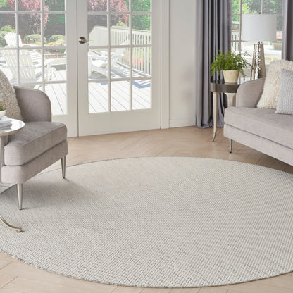 Circular light beige rug in a bright modern living room with gray sofa, armchair, plant, curtains, and glass patio doors.