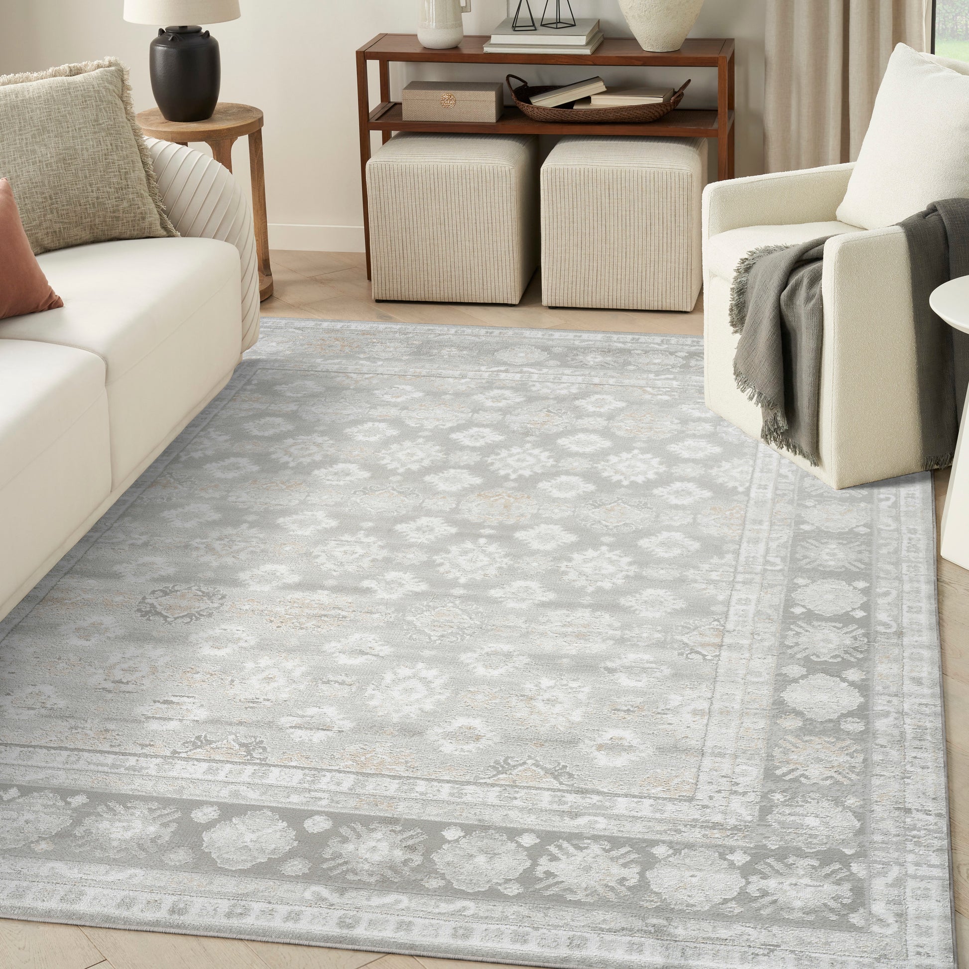 Light gray oriental area rug with ivory border in a cozy living room with cream sofa, beige ottomans, and wood console.