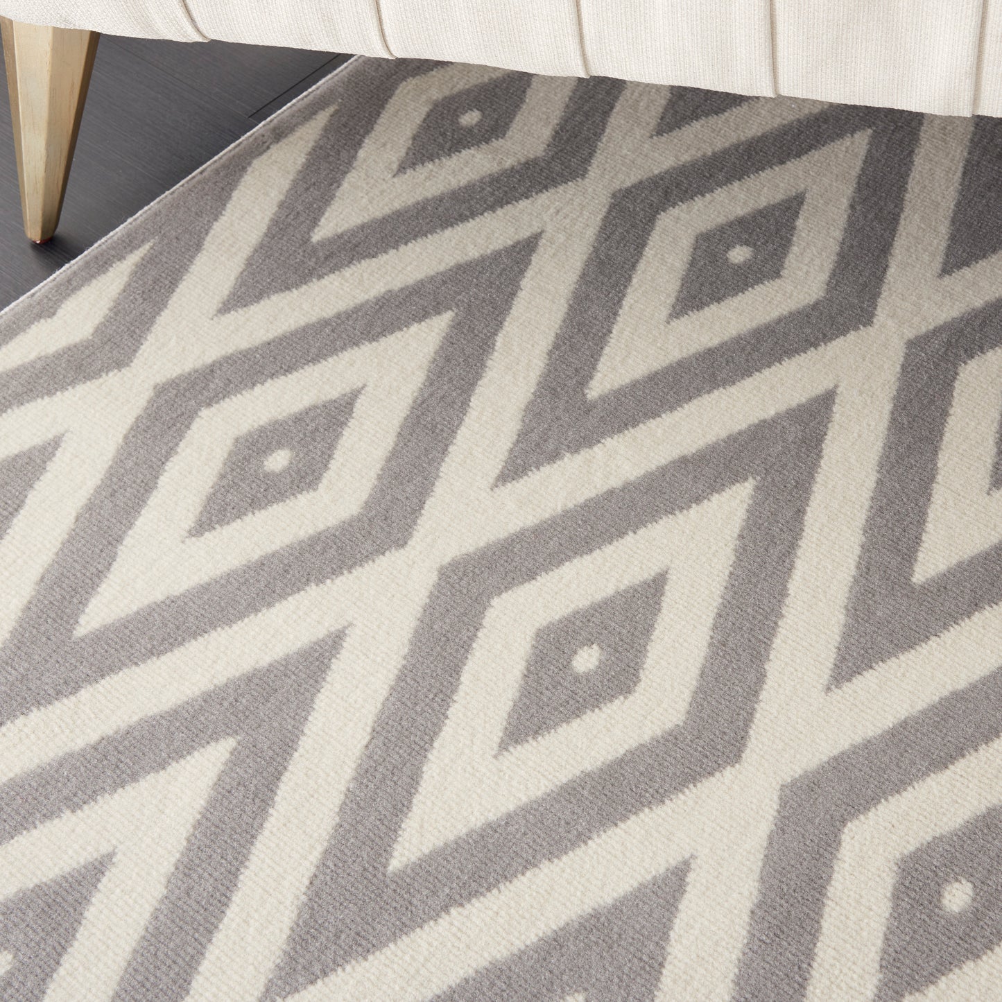 Gray and ivory diamond-pattern rug under a cream sofa, with a light wood furniture leg visible.