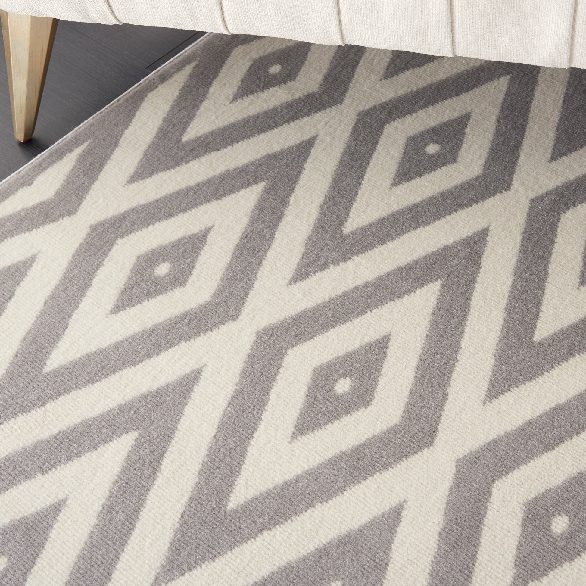 Gray and ivory diamond-pattern rug under a cream sofa, with a light wood furniture leg visible.