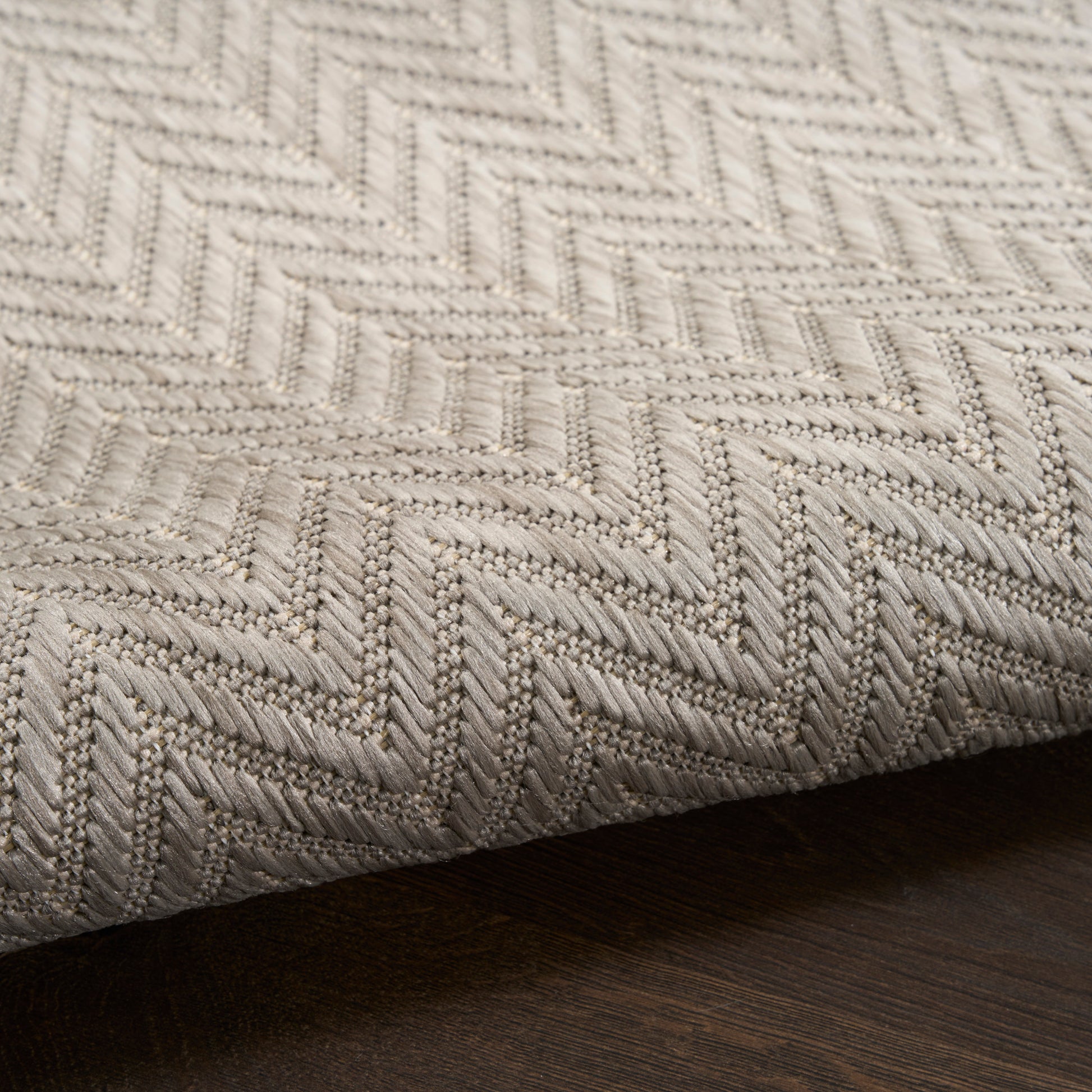 Beige chevron-weave rug with thick textured yarn on dark wood floor.