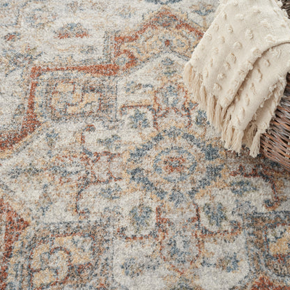 Vintage-style geometric patterned area rug in beige, blue and rust with a cream fringed throw over a wicker basket.
