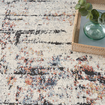 Beige abstract patterned rug with black and multicolor specks; wicker tray holding a green glass vase and eucalyptus leaves.