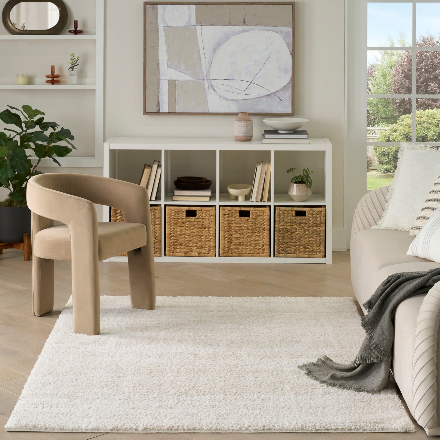 Neutral living room with white cubby console, woven baskets, abstract art, beige curved chair, plush white rug, plants.