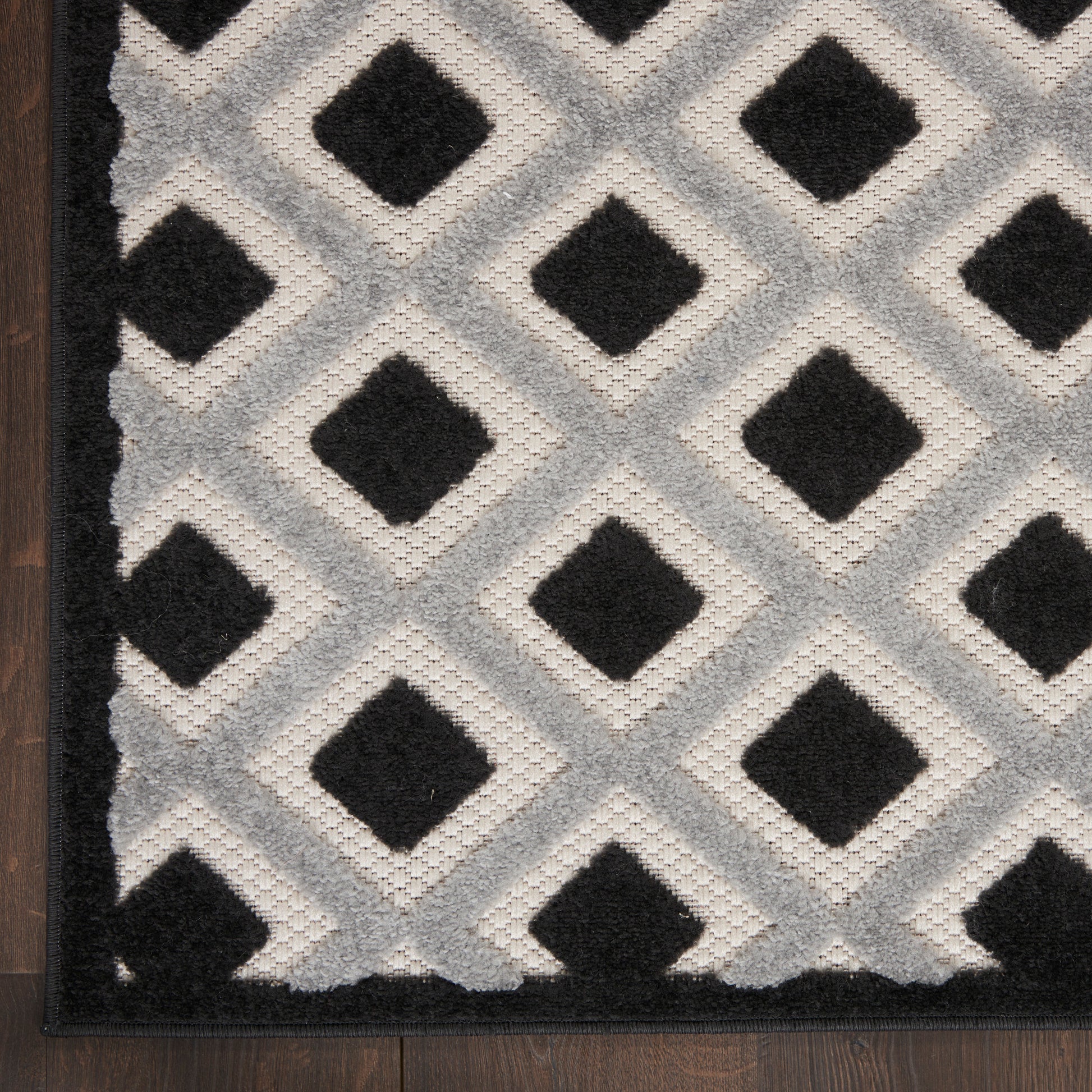 Gray and black diamond lattice runner rug with tufted pile and dark border on wood floor.
