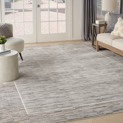 Gray-toned textured area rug in a bright living room with glass doors, beige sofa and round concrete coffee table.