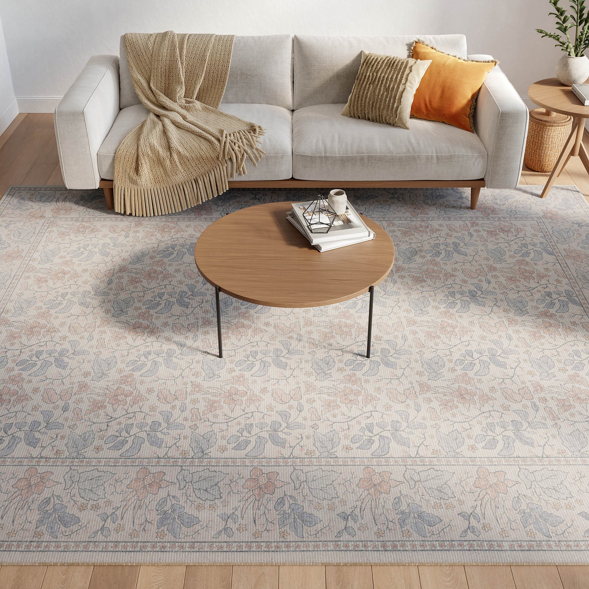 Living room with a light gray sofa, beige throw, orange cushions, round wooden coffee table, and pastel floral rug.
