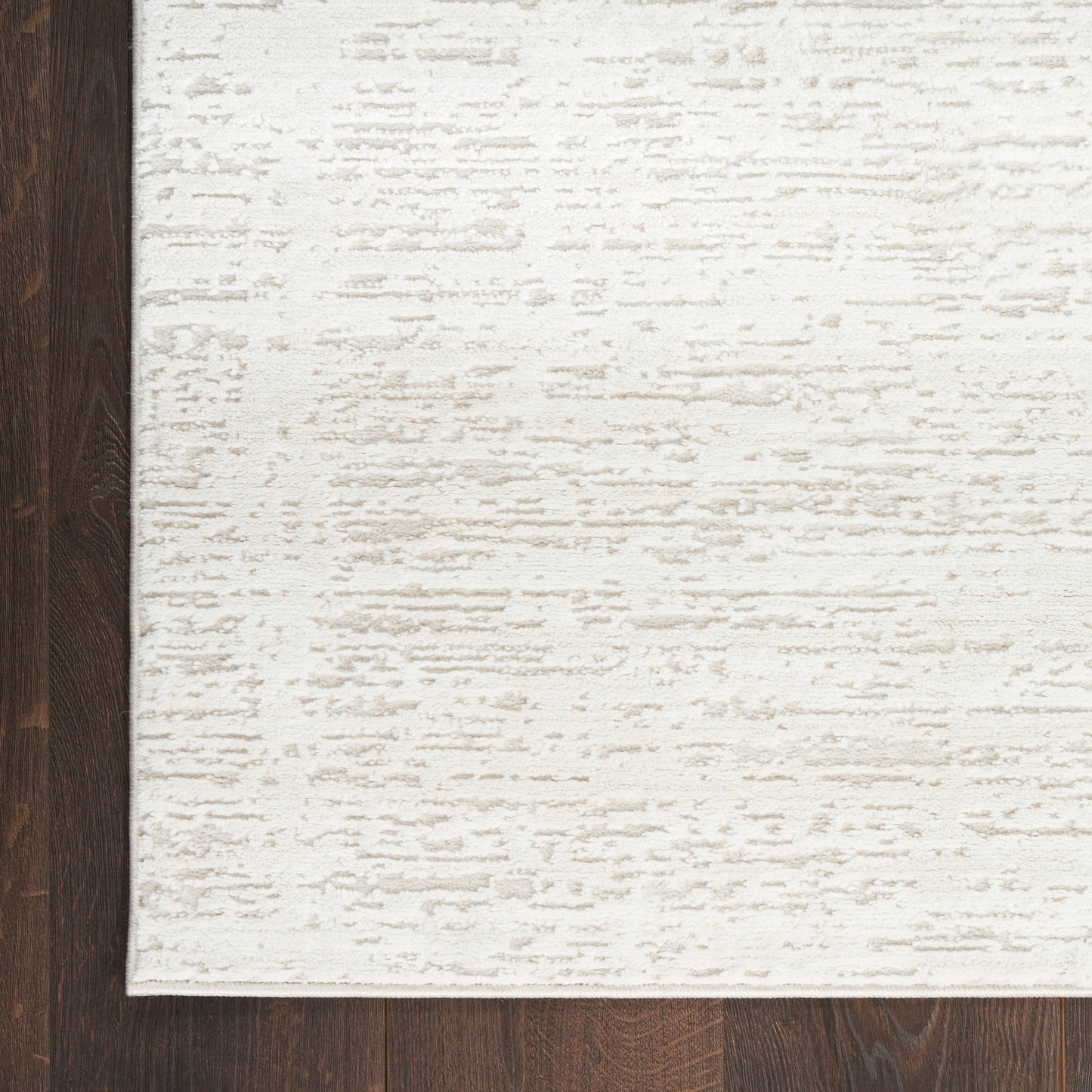 Cream textured area rug with subtle distressed pattern on dark brown hardwood floor.