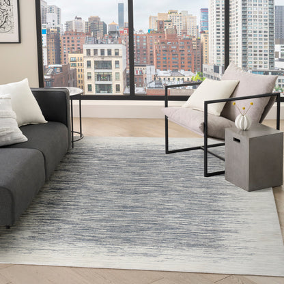 Modern living room with cityscape window, gray sofa, metal-framed chair, geometric rug, and concrete side table with white vase.