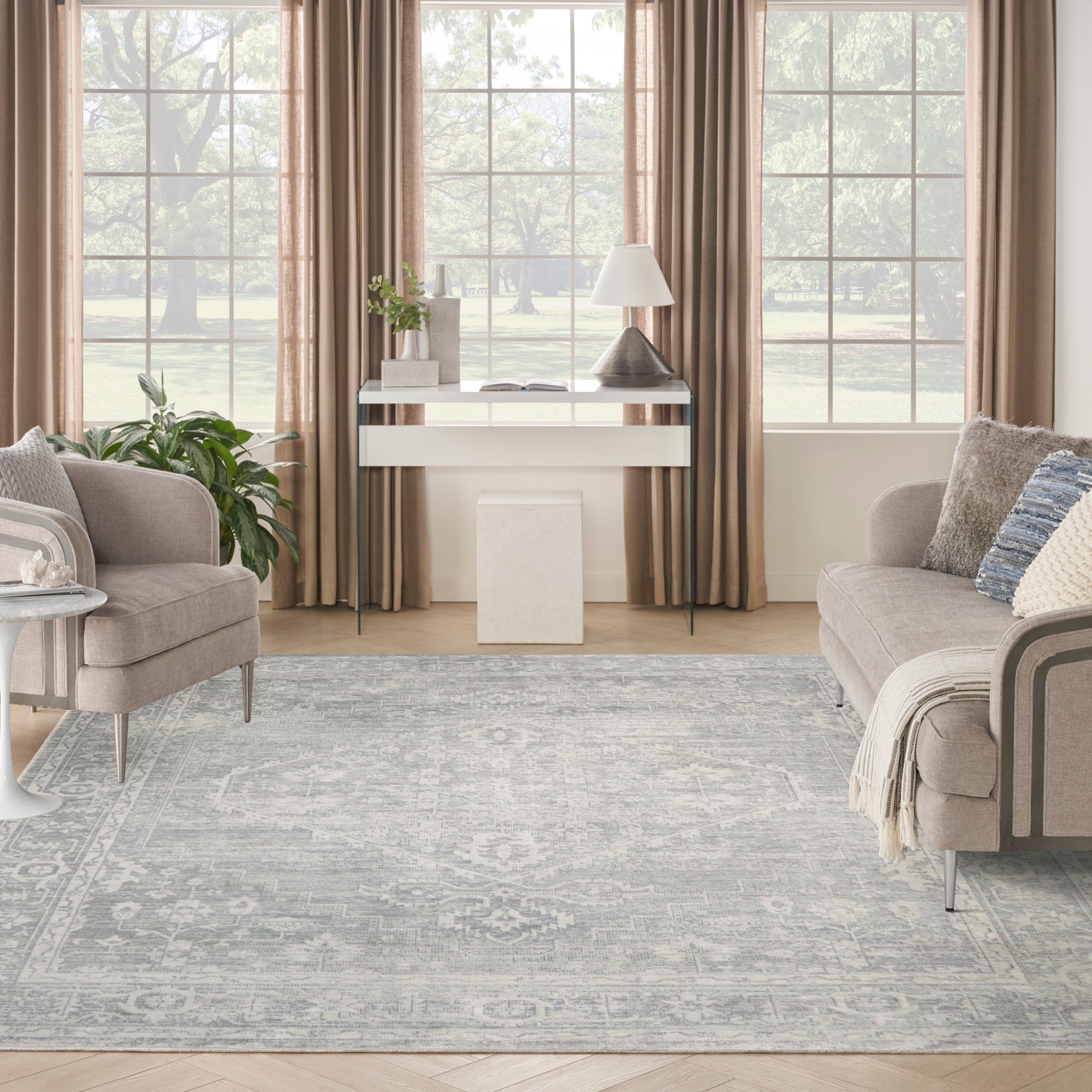 Neutral living room with taupe curtains, glass console table, lamp, plant, beige sofa and armchair, blue-gray rug.