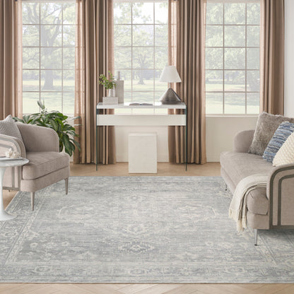 Neutral living room with taupe curtains, glass console table, lamp, plant, beige sofa and armchair, blue-gray rug.