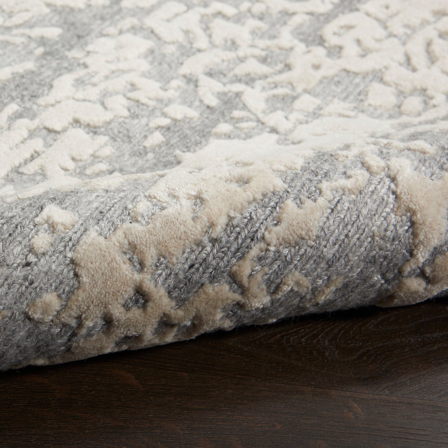 Gray and beige abstract-patterned plush rug with soft pile, folded edge on dark wood floor.