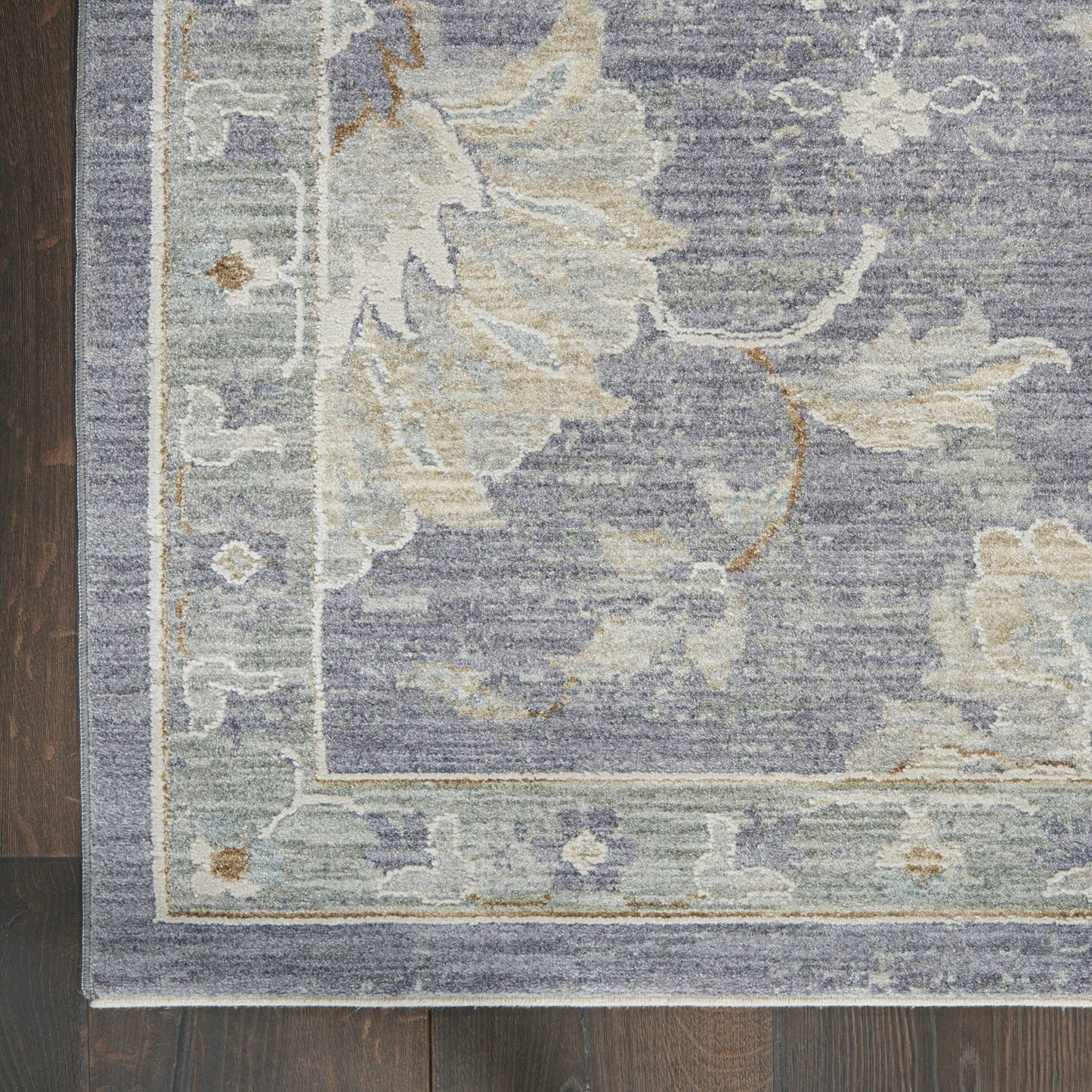 Blue-gray woven area rug with ivory floral motif and light border, damask-style pattern on dark wood floor.