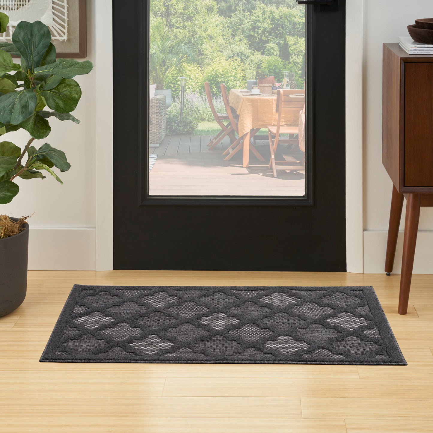 Dark gray rectangular doormat with diamond lattice pattern in front of a glass door on light wood floor.