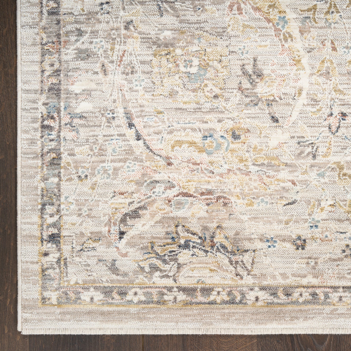 Cream-toned oriental rug with a distressed floral medallion, pale blue and gold accents, fringed edge on dark wood floor.