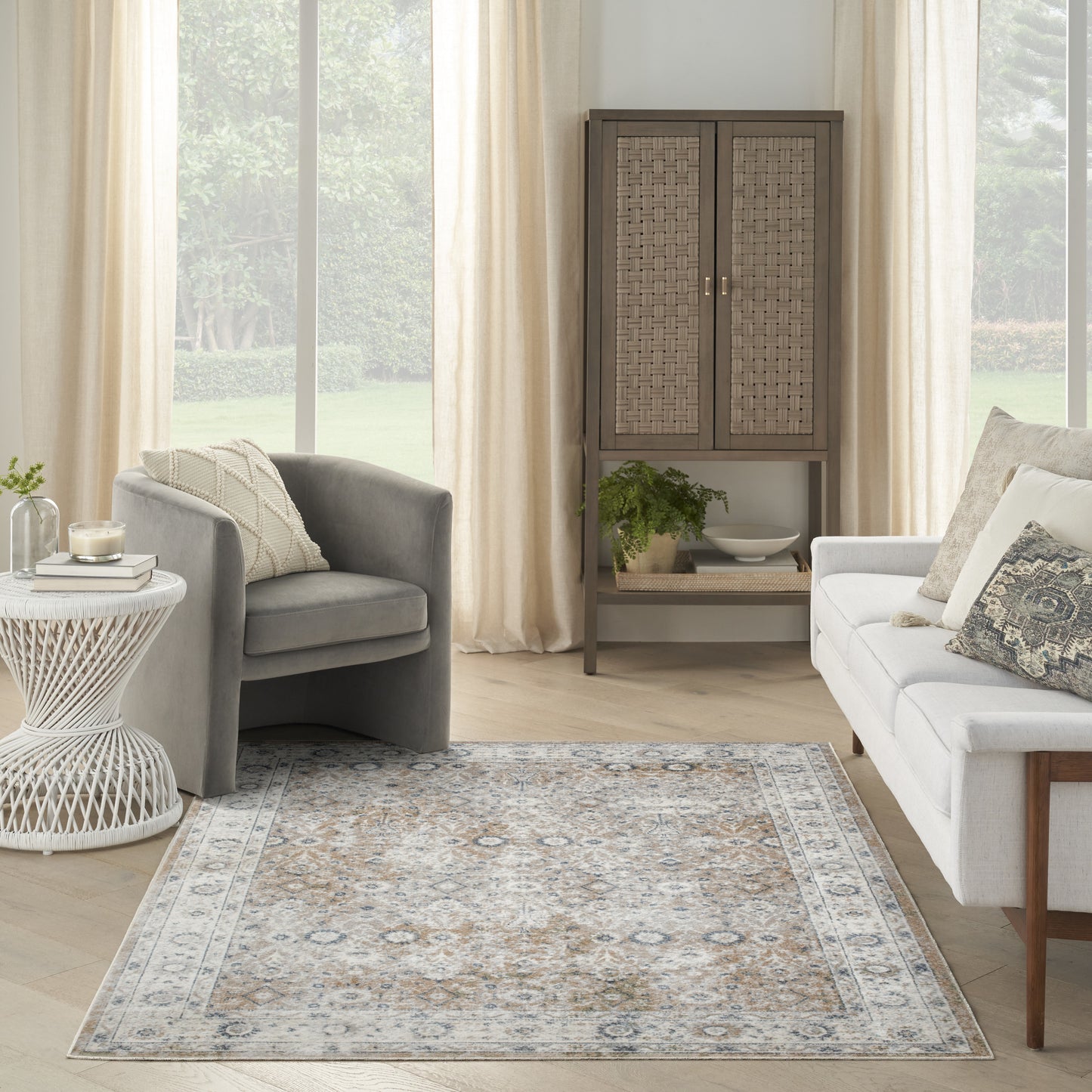 Cozy living room with pale-blue and beige ornate rug, gray armchairs, white sofa, woven cabinet, neutral curtains.