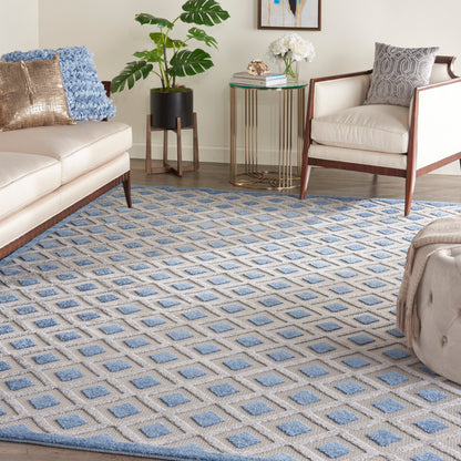 Living room with blue diamond-pattern rug, beige sofa and armchairs, gold glass side table, potted plant, and pillows.