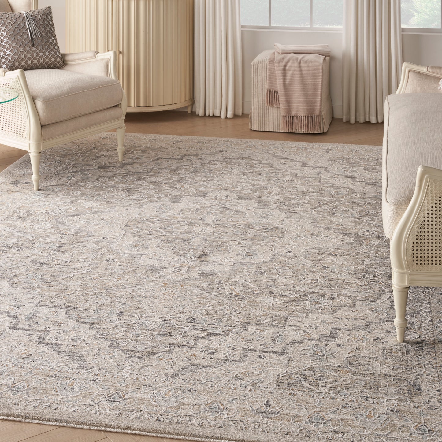 Cream-beige patterned area rug with subtle geometric medallions in a serene living room with cream upholstered chairs.