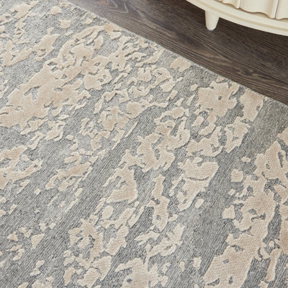 Gray and beige abstract-patterned area rug with a distressed look on a dark wood floor beside a cream-colored furniture leg.