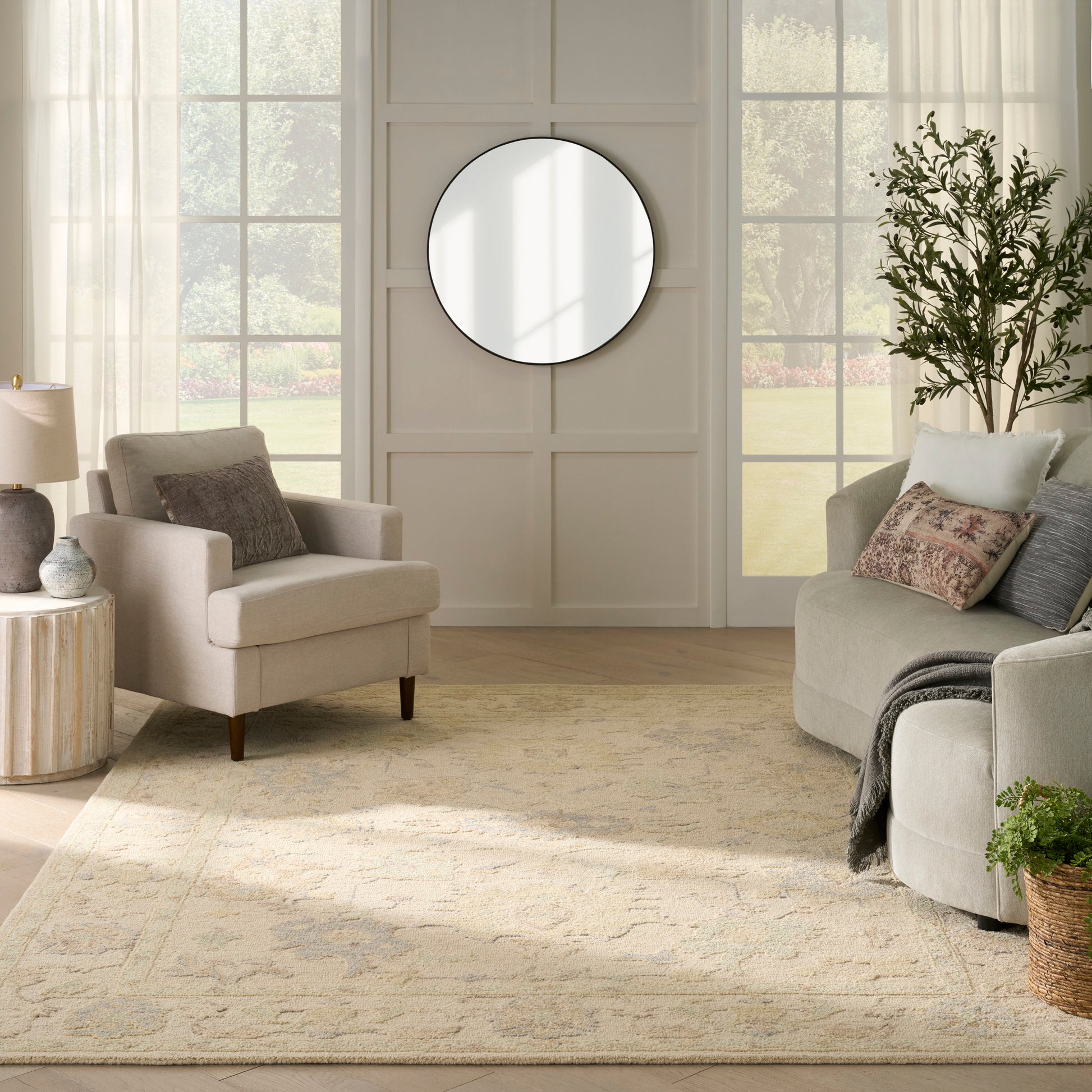 Bright living room with a round black-framed mirror on paneled wall, beige sofa and armchairs, cream area rug, potted plant.