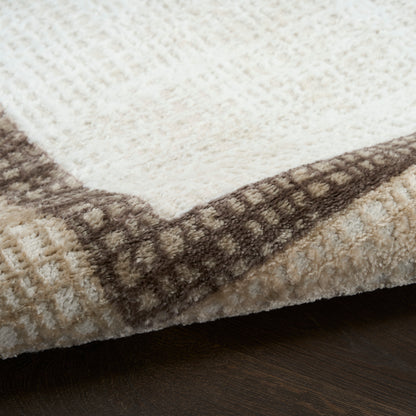 Close-up of a cream and brown plush area rug with a geometric border, soft pile, resting on dark wood floor.