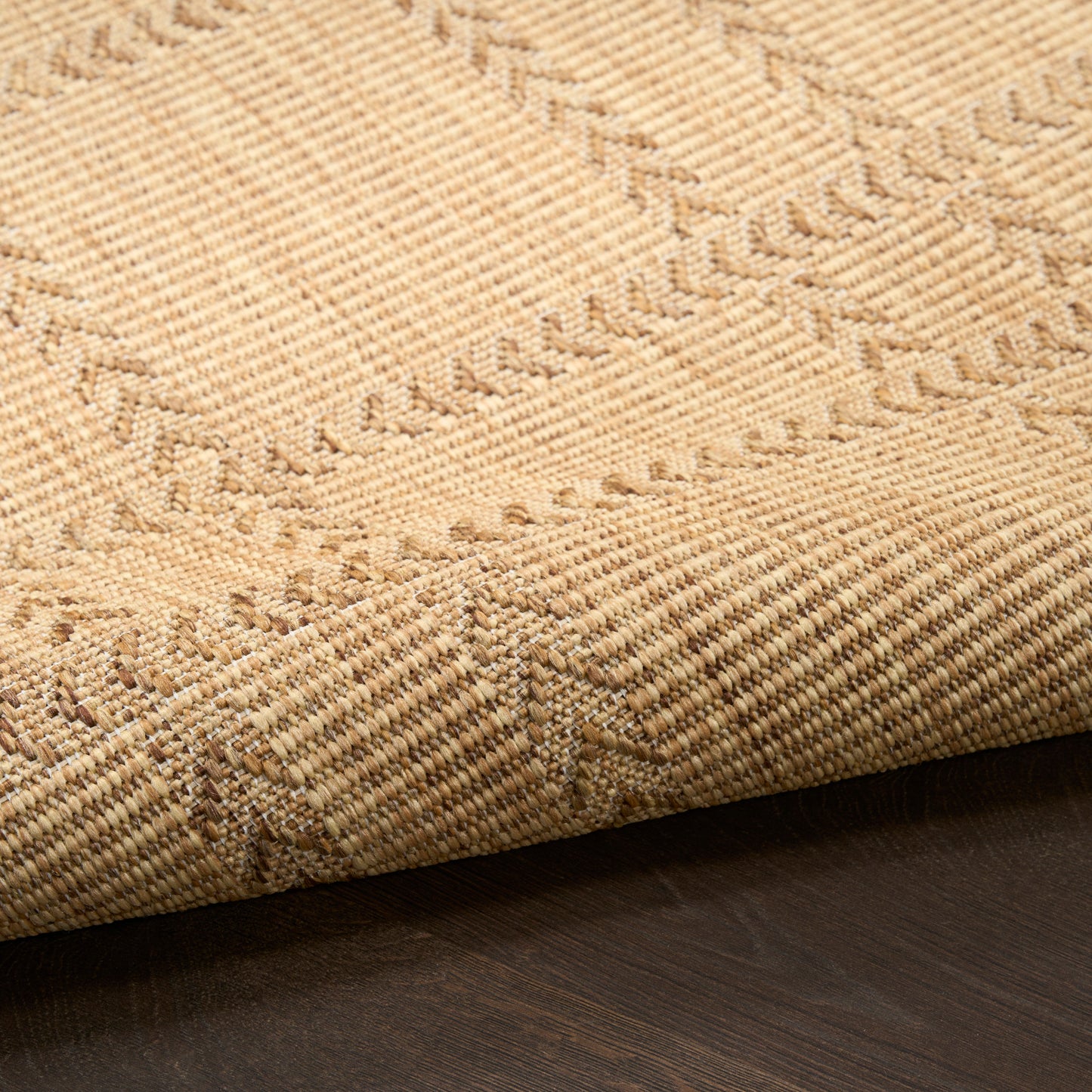 Beige natural-fiber rug with geometric chevron pattern, woven texture, folded edge on dark wood floor