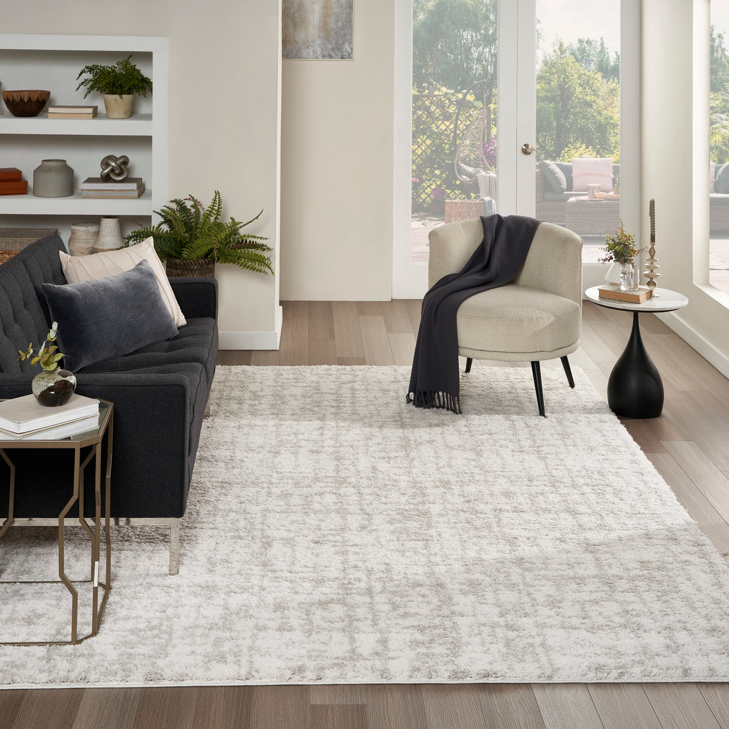 Modern living room with dark gray fabric sofa, beige accent chair, light rug, wood floors, and gold metal side tables.