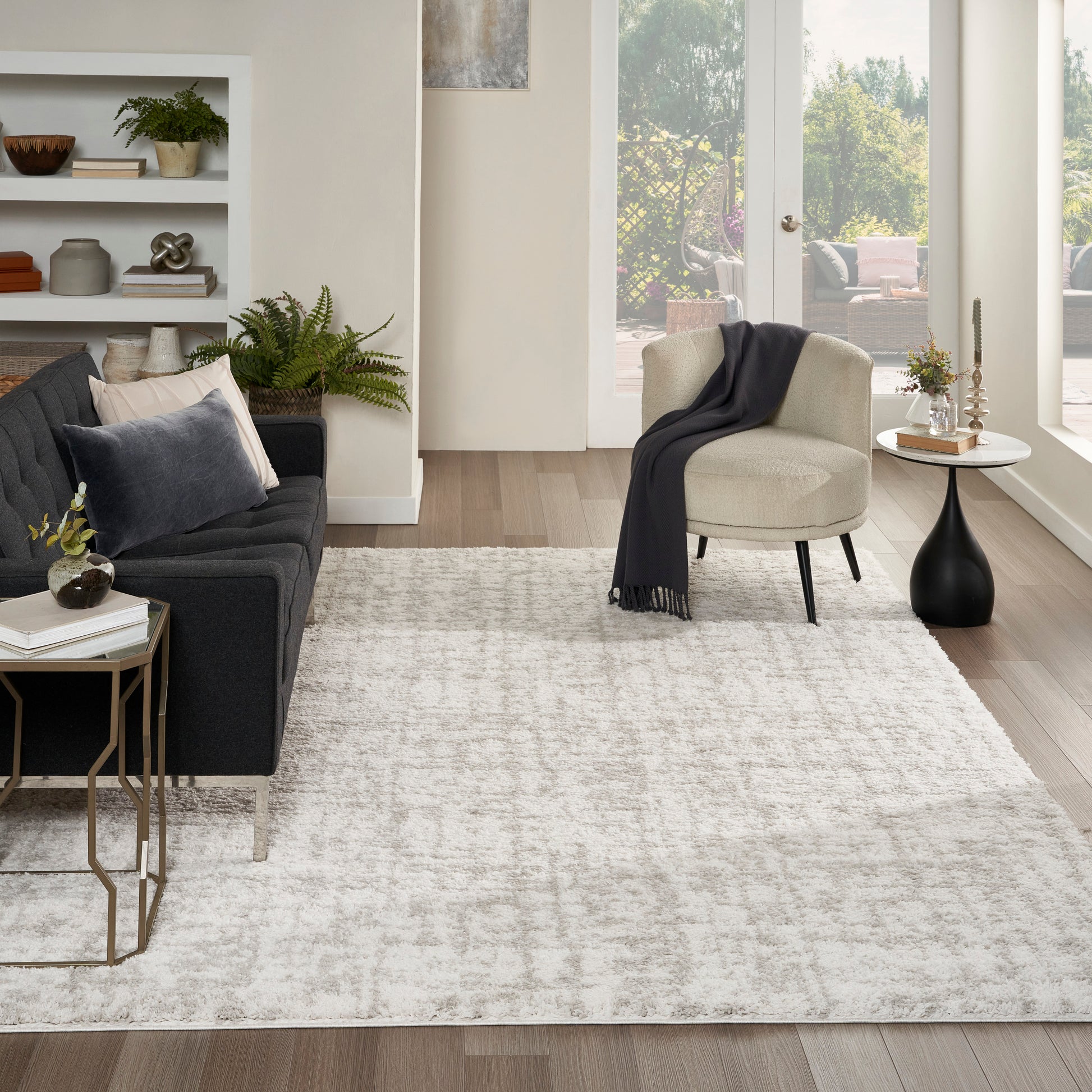 Modern living room with dark gray fabric sofa, beige accent chair, light rug, wood floors, and gold metal side tables.