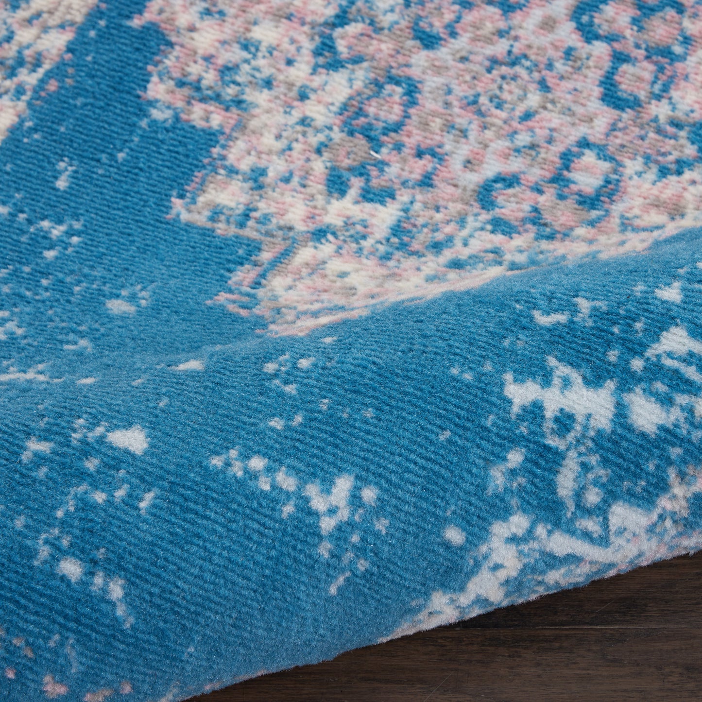 Turquoise blue distressed vintage rug with pink and cream marbling, soft woven texture on wood floor.
